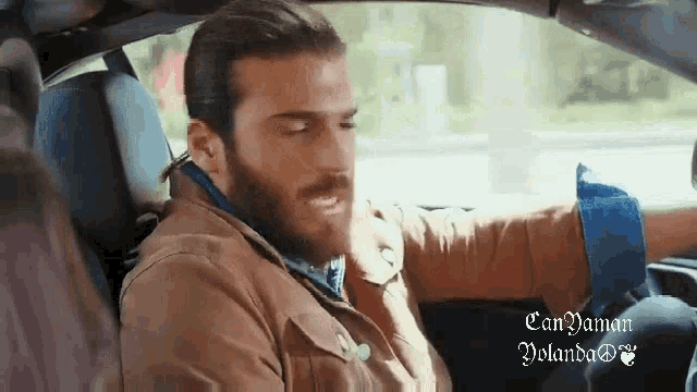a man with a beard is sitting in the driver 's seat of a car