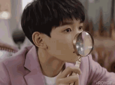a young man is looking through a magnifying glass at something .