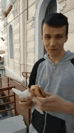 a man in a hoodie is eating a sandwich outside