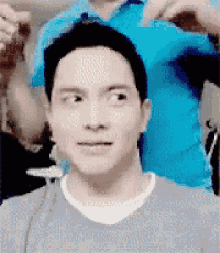 a man is getting his hair cut by a man in a blue shirt while making a funny face .