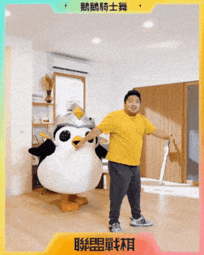 a man in a yellow shirt is standing next to a penguin mascot in a living room