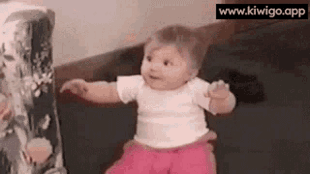 a baby in pink pants and a white shirt is sitting on the floor .