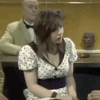 a woman in a polka dot dress is sitting at a table talking to a man in a tuxedo .