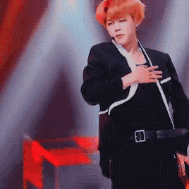 a man in a black suit is standing on a stage with his hands on his chest .