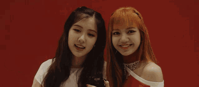 a couple of girls standing next to each other on a red background making a heart shape with their hands