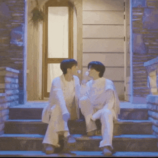 two men are sitting on the steps of a building drinking from a bottle .