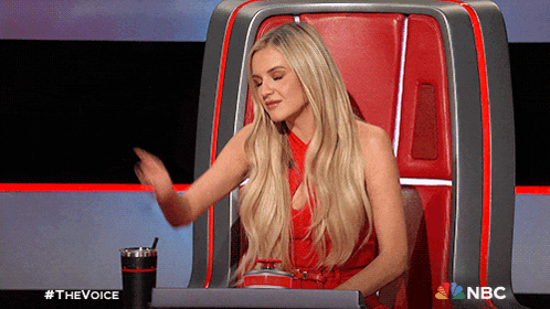 a woman in a red dress is sitting in a chair with a nbc logo on the bottom right