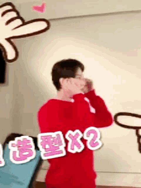 a man in a red sweater is standing in front of a wall and covering his face with his hands .