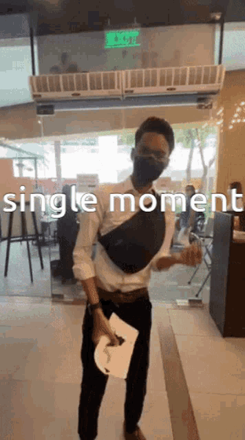 a man in a white shirt and black pants is wearing a mask and holding a piece of paper with the words single moment on it