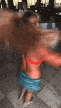 a woman in a red bikini top and blue shorts is dancing on a tiled floor .