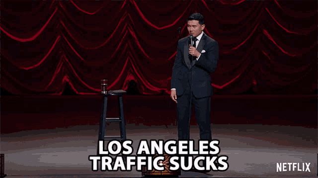 a man in a suit stands in front of a microphone with the words los angeles traffic sucks on the bottom