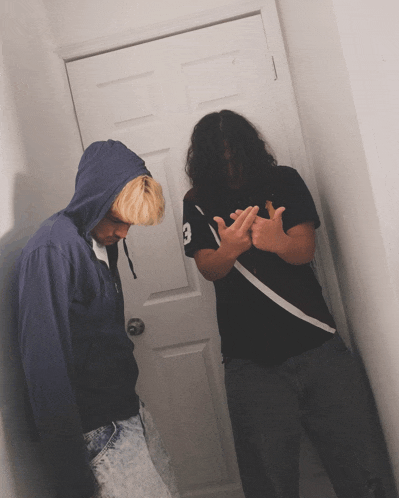 a man in a black shirt with the number 3 on it stands next to another man in a blue hoodie