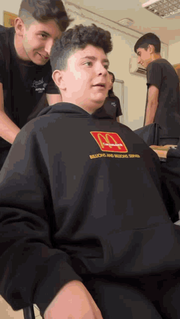 a boy wearing a black mcdonald 's hoodie is getting his hair cut