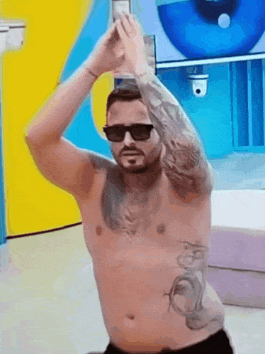 a shirtless man with tattoos on his arms and chest is wearing sunglasses and dancing .