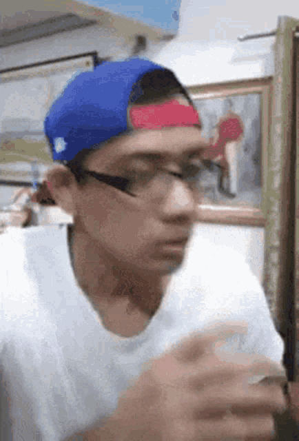 a young man wearing a blue hat and glasses is looking at his phone .