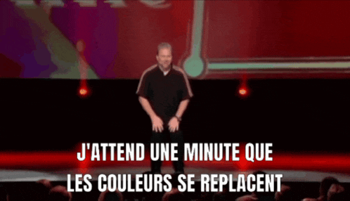 a man stands on a stage with the words " j'attend une minute que les couleurs se replacent " above him