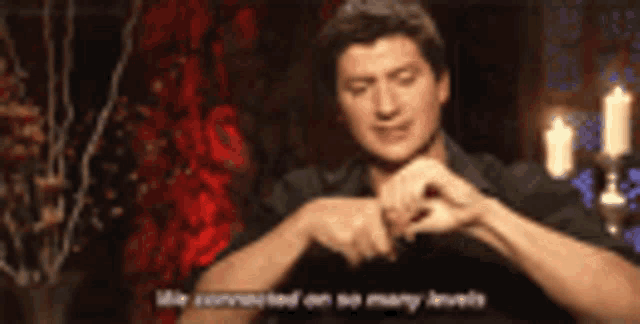 a man in a black shirt is sitting in front of candles and making a heart shape with his hands