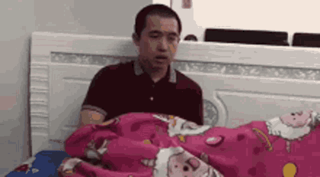 a man is laying in bed with a pink blanket .