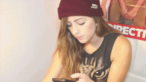 a woman wearing a beanie and a cat shirt looks down at her phone