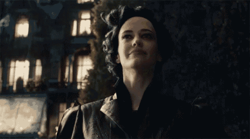 a woman in a black coat is smiling in front of a dark building .