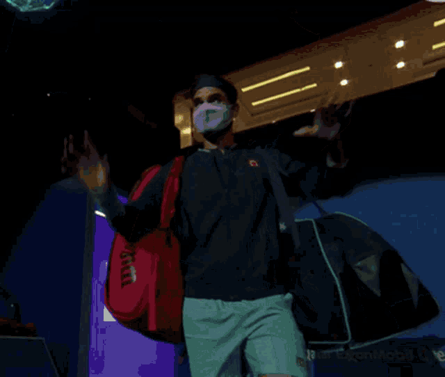 a man wearing a mask holds up his hand in front of a screen that says ' tokyo olympics ' on it