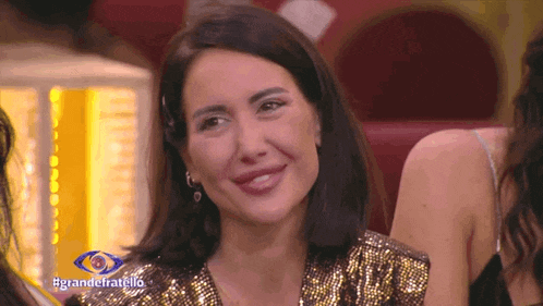 a woman in a gold sequined top is smiling in front of a sign that says grande fratello