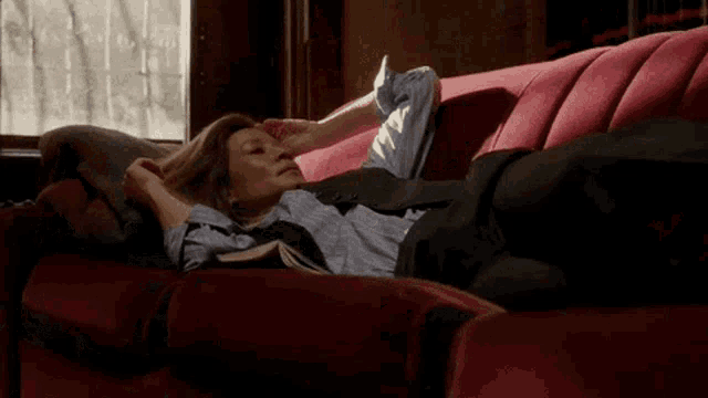 a woman is laying on a red couch with a book on her lap