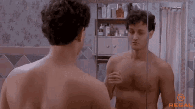 a shirtless man is looking at himself in a mirror in a bathroom .