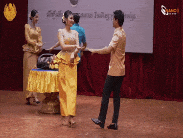 a man and a woman are dancing in front of a screen that says nano online