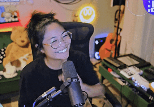 a woman with glasses is smiling in front of a microphone with the letter w on the wall behind her