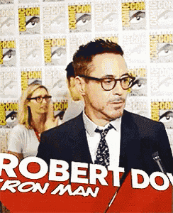 a man in a suit and tie stands in front of a sign that says " robert downey jr. "