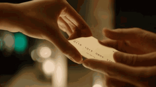 a person is handing a credit card to another person with the numbers 0116 and 1013