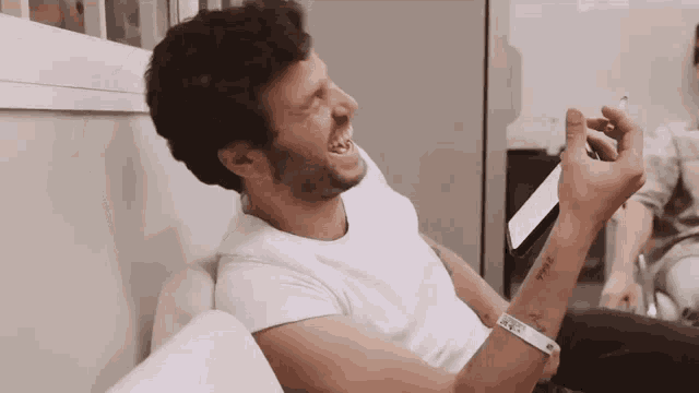 a man sitting on a couch laughing with a wristband that says ' a ' on it