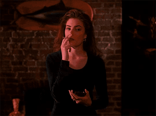 a woman in a black shirt stands in front of a brick wall holding something in her hands
