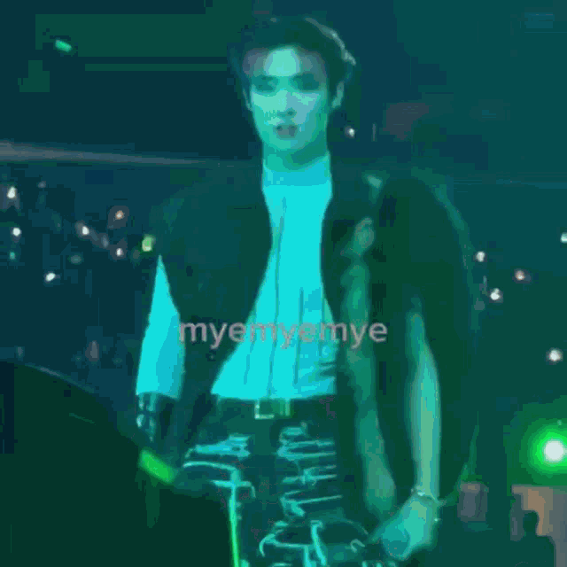 a man in a black jacket stands on a stage in front of a crowd with the words myem on the bottom