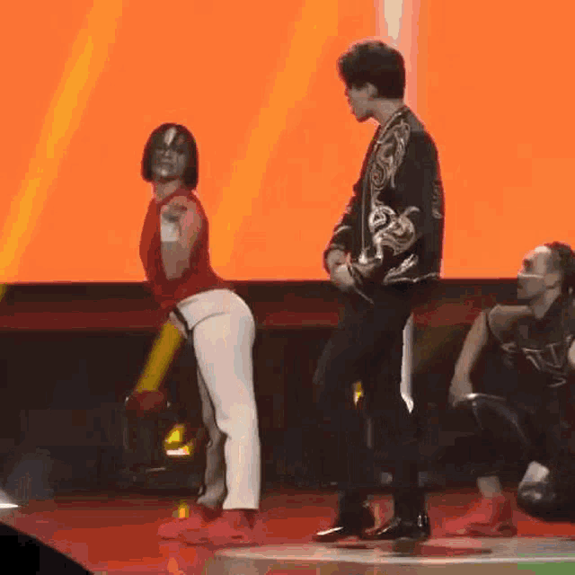 a man and a woman are dancing on a stage . the woman is wearing a red top and white pants .