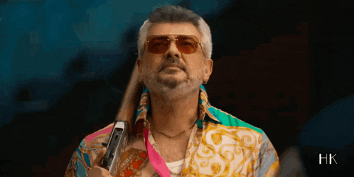 a man with a beard wearing sunglasses and a colorful shirt is holding a gun .