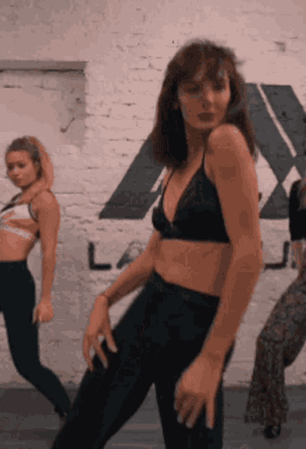 a woman in a black bra is dancing in front of a brick wall with the letter l on it