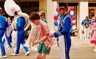 a man in a marching band is helping a boy carry a french horn in a parade .