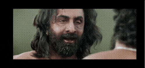 a man with long hair and a beard is looking at another man .