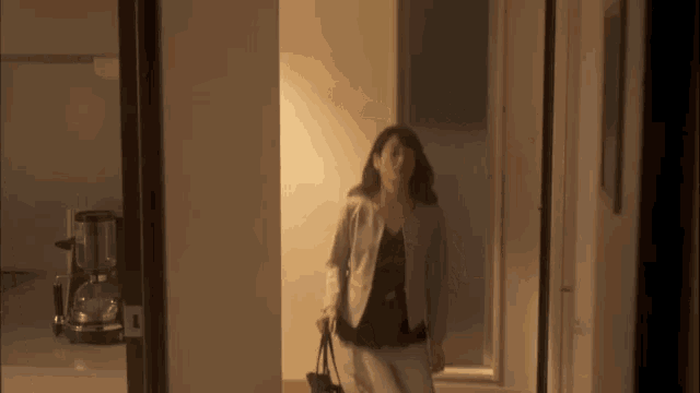 a woman in a suit is walking down a hallway with a purse .