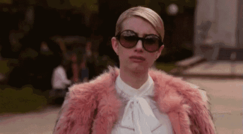a woman wearing a pink fur coat and sunglasses is standing on a sidewalk .