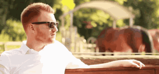 a man wearing sunglasses and a white shirt leans on a wooden fence