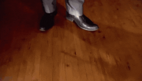 a man in a suit is standing on a wooden floor smoking a cigarette .