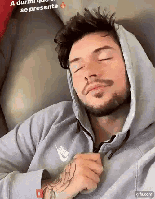 a man wearing a nike hoodie sleeping on a couch