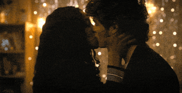a man and a woman are kissing in front of a wall of lights