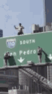 a man is standing on top of a green highway sign that says 110 south san pedro .