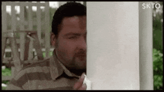 a man is peeking out from behind a white pole .