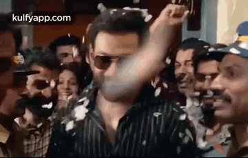 a man in sunglasses is standing in front of a crowd of people and throwing confetti .