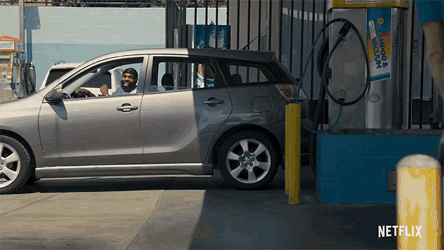 a man is driving a car at a gas station with a netflix logo on the bottom right